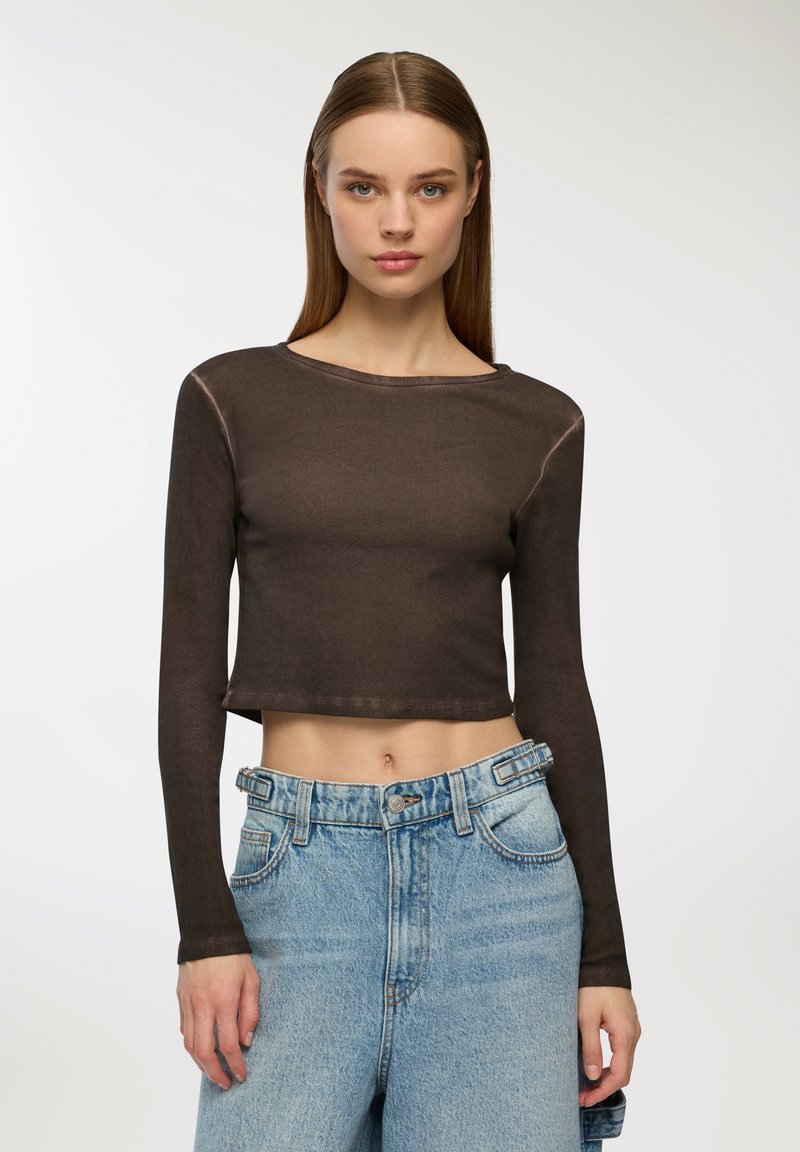 Brązowy, długi rękaw, krótki top z okrągłym dekoltem, wykonany z gładkiego, elastycznego materiału, połączony z jasnoniebieskimi spodniami z wysokim stanem.