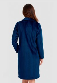 Bata de baño de terciopelo azul marino que presenta un cuello, mangas largas y un patrón de rayas texturizadas. Llega hasta la mitad del muslo con un dobladillo recto.
