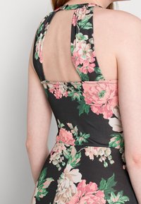 Robe à imprimé floral avec un fond noir. Elle présente un col halter, un dos nu et des motifs floraux roses et verts sur un matériau doux.