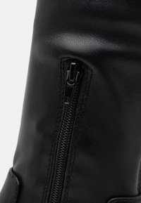 Black leather boot featuring a side zipper, smooth texture, and reinforced stitching. The design includes a subtle sheen and a sturdy sole.