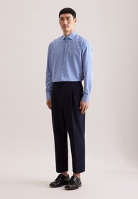 Koszula na guziki w niebieskie i białe paski z długimi rękawami, zestawiona z ciemnymi spodniami i czarnymi butami na sznurowadła, stojąca na neutralnym tle.