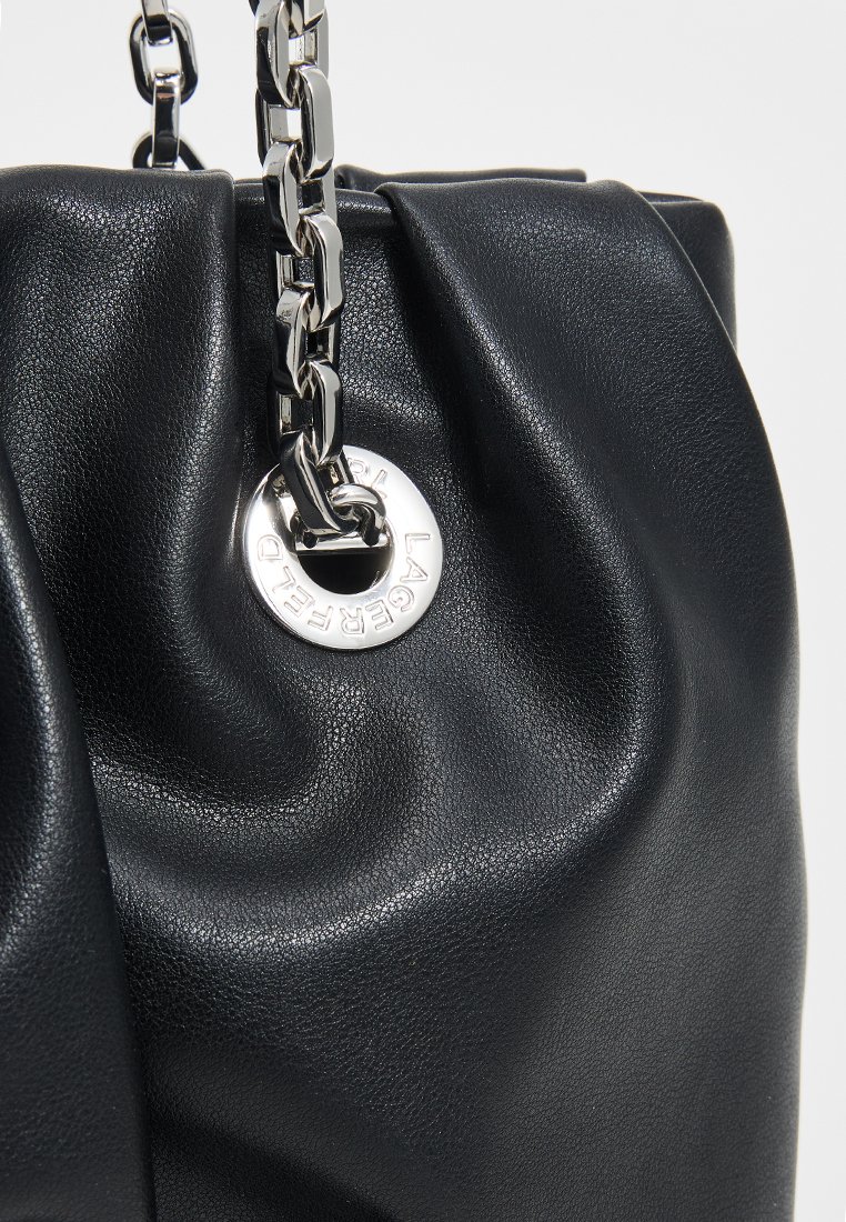 Bolso de mano de cuero negro con una textura suave y arrugada. Presenta un logo circular plateado y un asa de cadena de metal grueso.