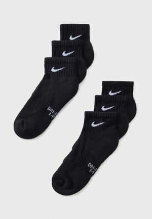 Zes zwarte Nike enkelsokken met witte Swoosh-logo's, gerangschikt in twee rijen van drie paar op een lichte achtergrond.