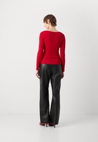 Haut à manches longues rouge côtelé avec un décolleté carré, associé à un pantalon en cuir noir taille haute. La tenue présente une silhouette ajustée.