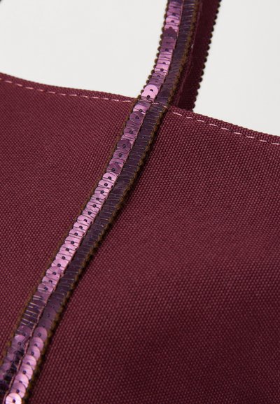 Maroon handbag with a textured fabric body, featuring a shiny purple sequin strap and contrasting brown stitching along the seam.