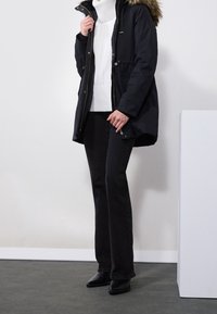 Granatowa parka z kapturem obszytym futrem, biały golf i czarne dzwony. Złote dodatki i taliowany krój. Czarne botki za kostkę.