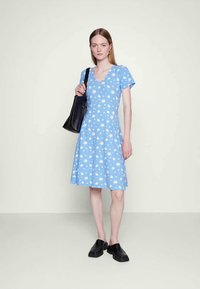 Vestido azul claro com estampa floral branca, mangas curtas e decote em V, com evasé na cintura. Combinado com uma bolsa tote preta e sapatos slip-on pretos.