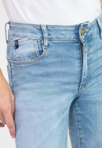 Lichtblauwe denim jeans met een hoge taille, een ritssluiting en vijf zakken. Bevat stikselaccenten en een klein merklabel op de tailleband.
