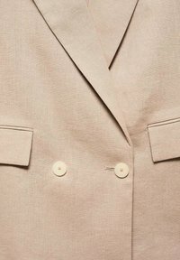 Blazer beige in lino con design doppiopetto, revers, e due tasche frontali con grandi bottoni rotondi.