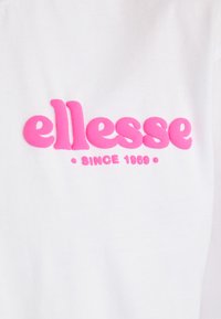 T-shirt en coton blanc arborant un logo "ellesse" rose vif avec une police arrondie et "SINCE 1959" en dessous dans une police plus petite.