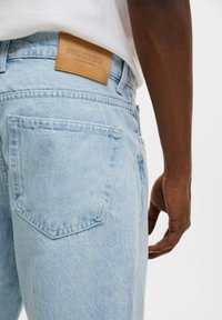 Los jeans de mezclilla azul claro presentan un acabado texturizado, un bolsillo trasero y una etiqueta de cuero marrón con "PULL&BEAR" grabado en la cintura.