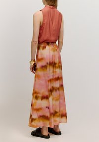 Maxi-jurk met een roze-oranje tie-dye patroon, met een textuurrijke mouwloze top en een vloeiende rok. Gemaakt met zwarte sandalen.