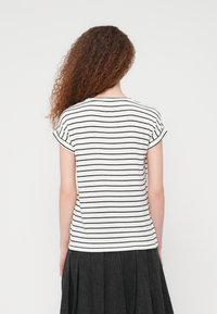T-shirt rayé avec base blanche et lignes horizontales noires, doté de manches courtes retroussées et d'une coupe décontractée. La longueur atteint la ligne de la taille.