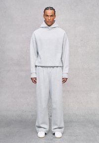 Sudadera gris clara y pantalones de chándal a juego, hechos de una tela suave. Corte holgado con un bolsillo canguro y puños acanalados. Zapatillas blancas completan el look.