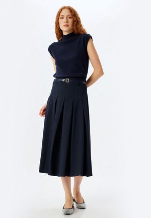 Top senza maniche blu navy, gonna plissettata blu navy con cintura e scarpe a disegno bianco e nero. Tessuto liscio, silhouette fino al ginocchio.