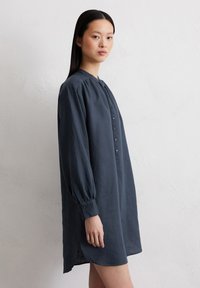 Donkerblauwe linnen jurk met lange mouwen, knoopsluiting aan de voorkant en zijsplitten; relaxte pasvorm en lichte textuur.