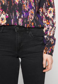 Blusa de manga larga multicolor con patrones abstractos combinada con jeans de mezclilla negros. La tela es lisa con un ligero brillo.