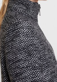 Maglione con zip nera e grigia. Motivo a maglia texture con colletto alto. Tessuto morbido e caldo con una silhouette aderente.