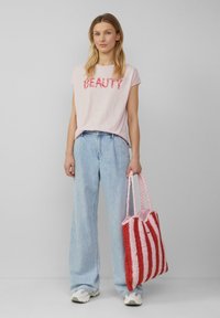 Lichtroze katoenen T-shirt met "BEAUTY" in het rood gedrukt, gecombineerd met wijde blauwe spijkerbroek en een rood-roze gestreepte geweven tas.