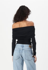 Melna off-the-shoulder blūze ar garām piedurknēm un drapēta tekstūra, apvienota ar gaiši ziliem augsta jostas izmēra džinsiem ar aizmugurējām kabatām un zīmolu.