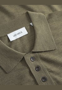 Olijfgroene poloshirt van een gestructureerde brei, met een platte kraag en drie donkere knopen. Het etiket zegt "LES DEUX."
