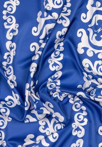 Tissu bleu à texture brillante, présentant un motif tourbillonnant blanc sur toute la surface. Le design est symétrique et offre un contraste marqué.