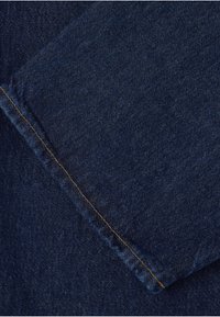 Gros plan d'un tissu en denim bleu foncé avec une couture diagonale visible cousue à fils orange.
