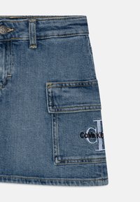 Džínová sukně ve středně modré barvě s mírně opraným vzhledem. Má přední kapsu a vyšívané logo "Calvin Klein".