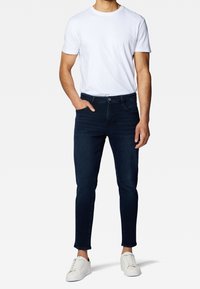 Mörkblå slim-fit jeans med en slät textur, med framfickor och dragkedja, kombinerade med en enkel vit T-shirt och vita sneakers.