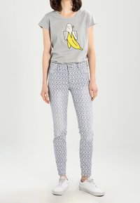 Camiseta gris de manga corta con un estampado de un personaje de plátano, combinada con leggings blancos con patrones y zapatillas blancas. Look simple y casual.