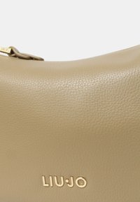 Borsa a tracolla in pelle beige chiaro con finitura testurizzata, caratterizzata da hardware dorato e un logo in rilievo sul davanti. Design curvo e liscio.
