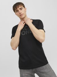 Black short-sleeve t-shirt with a matte logo print. Made of cotton, it features a crew neckline and a fitted design. Model has short hair.
