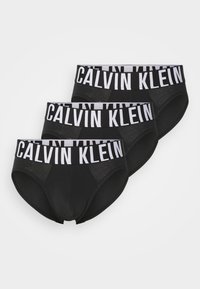 Drie paar zwarte katoen onderbroeken met een witte elastische tailleband waarop "CALVIN KLEIN" in dikke letters is gedrukt.