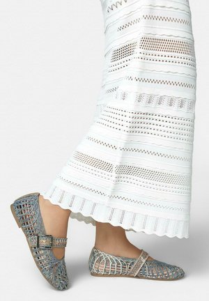 Füße in silbernen gewebten flachen Schuhen mit Schnalle und Riemen, kombiniert mit einem weißen, gehäkelten knöchellangen Rock.