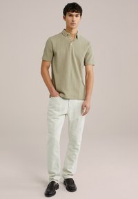 Light green, ribbed polo shirt with a collar and two buttons, paired with light, straight-leg jeans and black loafers. Simple design.