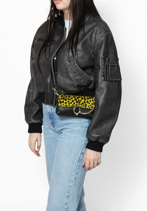 Giacca bomber nera in pelle cropped, jeans azzurri, e una pochette a stampa leopardata nera e gialla con dettaglio in catena.