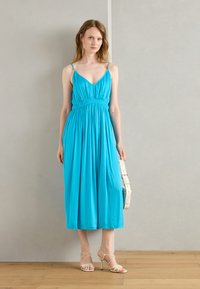 A flowing, ankle-length dress in vibrant turquoise, featuring spaghetti straps, a cinched waist, and soft, textured fabric.