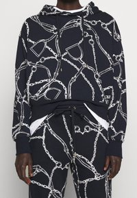 Marinblå hoodie med vitt kedjemönster, dragsko i luvan, känguruficka och ribbade ärmslut. Mjuk tyg med avslappnad passform, passar bra med matchande byxor.