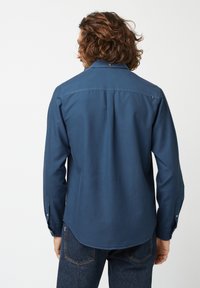 Blaue Baumwollhemd mit langen Ärmeln, spitzem Kragen und abgerundetem Saum, mit Knöpfen an den Manschetten und einem einzelnen Knopf hinten.