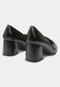 Chaussures à talons noirs avec une finition en cuir lisse, un bout arrondi et un talon bloc épais pour plus de stabilité. Des surpiqûres décoratives sont visibles.
