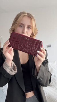 Bordeauxrode portemonnee van namaakcrocodillenleer met een gladde textuur, rechthoekige vorm, ritssluiting en geperst merklogo aan de voorkant.