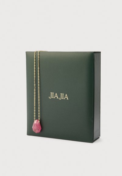 Grøn smykkeboks med guld "JIA JIA" mærkning, der indeholder en delikat guld kæde med en pink, facetcut sten vedhæng.