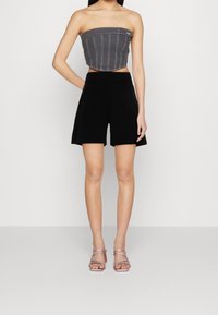 Haut court gris sans bretelles avec des coutures verticales, associé à un short taille haute noir. Le mannequin porte des talons rose à brides.