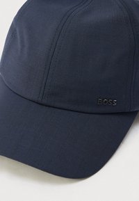 Tmavomodrá čiapka z hladkej látky s zakriveným šiltom a nenápadným logom "BOSS" na boku. Štruktúrovaný tvar s detailmi prešívania.