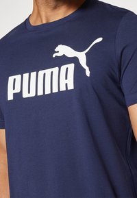 Camiseta de algodón azul marino con mangas cortas que presenta un gran logo blanco de "PUMA" y un gráfico de un puma saltando en blanco en la parte delantera.