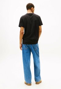 Zwart katoenen t-shirt met een klassieke ronde halslijn, gecombineerd met losse blauwe denim jeans. De jeans hebben achterzakken en een omgeslagen zoom.