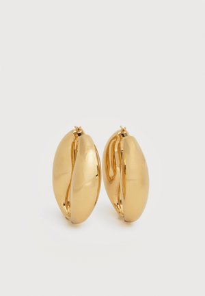 Paire de boucles d'oreilles épaisses en forme de créoles, effet or poli, avec un design légèrement ovale et massif, dotées de fermoirs à charnière sur fond blanc.