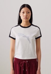White cotton T-shirt with black ribbed collar and sleeves, featuring a sparkling Puma logo on the front. Worn with burgundy joggers.