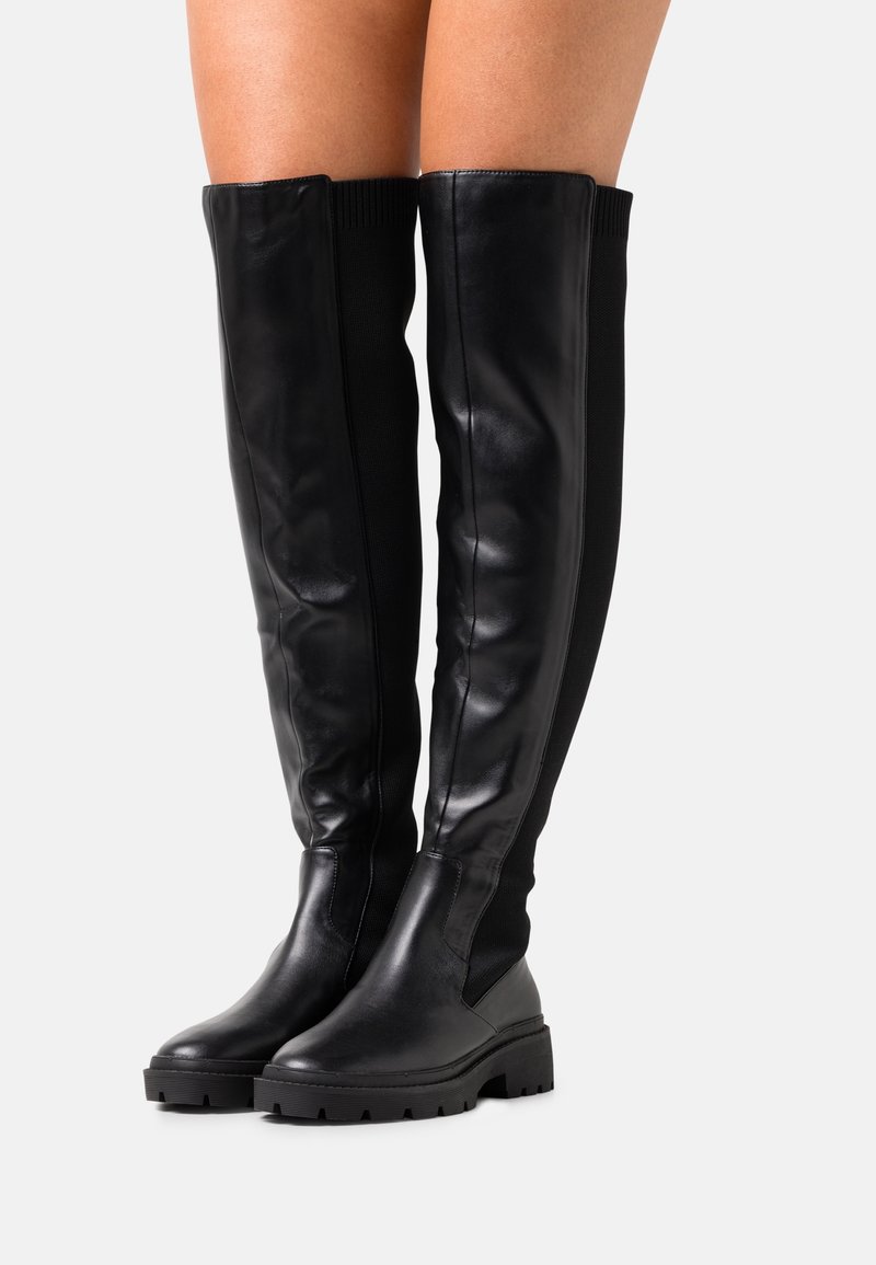 Bottes noires montantes au-dessus du genou avec un devant en cuir lisse, un dos en tissu côtelé et des semelles épaisses en caoutchouc avec des détails de crampons.