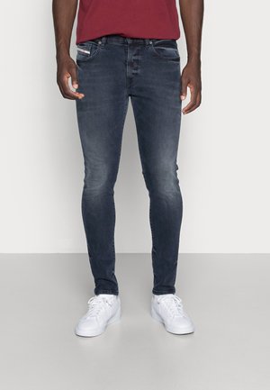Ciemnoniebieskie dżinsy o slim fit, z delikatnym wypłowieniem, pięcioma kieszeniami oraz kontrastowymi przeszyciami; zestawione z białymi trampkami.